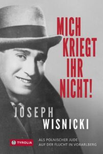 Okładka książki w odcieniach czerni, bieli i szarości przedstawia archiwalny portret uśmiechniętego młodego mężczyzny w jasnym kapeluszu i ciemnym płaszczu. Po prawej stronie, dużymi czerwonymi literami, widnieje tytuł: „Mich kriegt ihr nicht!” („Mnie nie dostaniecie!”). U dołu znajduje się nazwisko autora – Joseph Wisnicki – oraz podtytuł: Als polnischer Jude auf der Flucht in Vorarlberg („Jako polski Żyd na ucieczce w Vorarlbergu”). W lewym dolnym rogu umieszczono logo wydawnictwa Tyrolia.